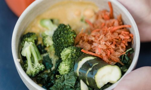 hands holding bowl of kimchi ramen with vegetables