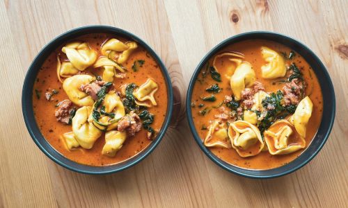 two bowls of tortellini soup on a table