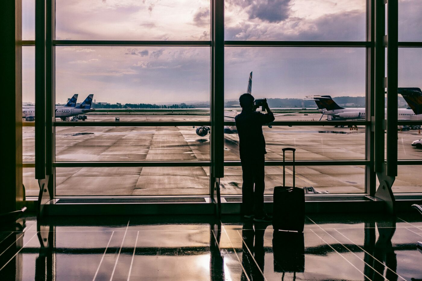 Man in airport lounge taking a picture of a plane out the window