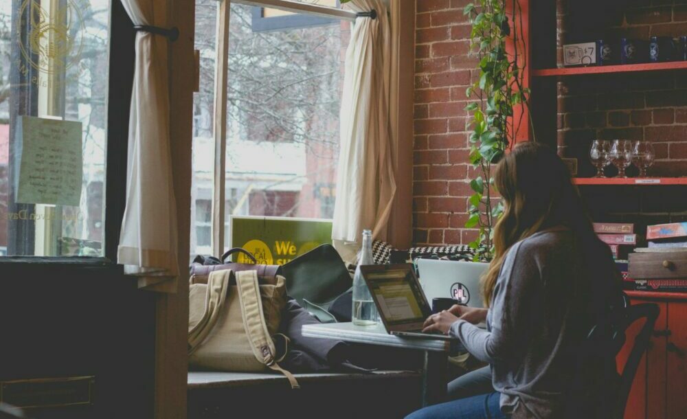 Student woman in coffee shop writing essay at her laptop