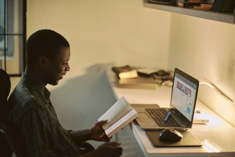 Student sat at laptop holding his book